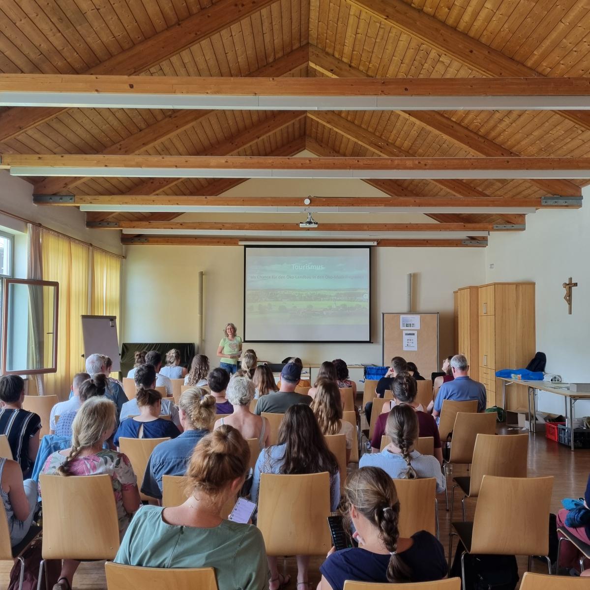 Menschen auf Stühlen sitzend in einem Seminarraum , die sich eine Präsentation auf einer Leinwand anschauen