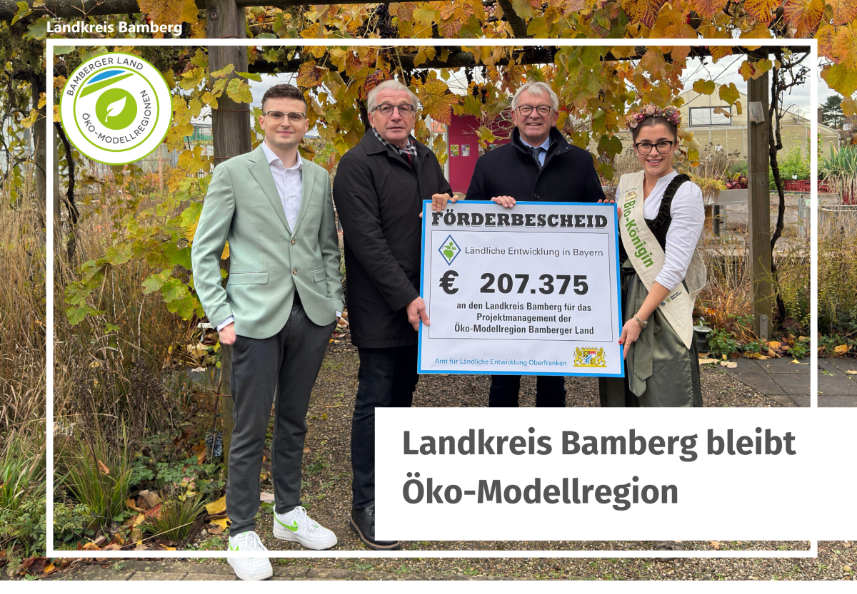 Personen halten ein Schild hoch. Darauf steht "Förderbescheid für den Kreis Bamberg)